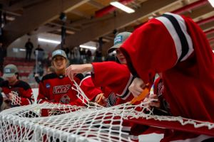 Hockey teammates in red jerseys gather around net during practice or game setup.