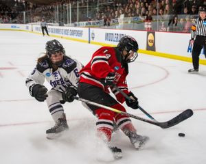 Two hockey players battle for the puck during an intense game, with one in white and one in red uniforms.