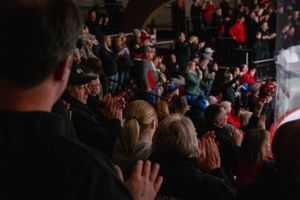 A crowd of spectators watching and cheering at an indoor sporting event with people wearing red apparel.