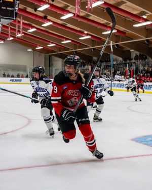 Hockey player in red jersey skating intensely during competitive ice hockey match on indoor rink.