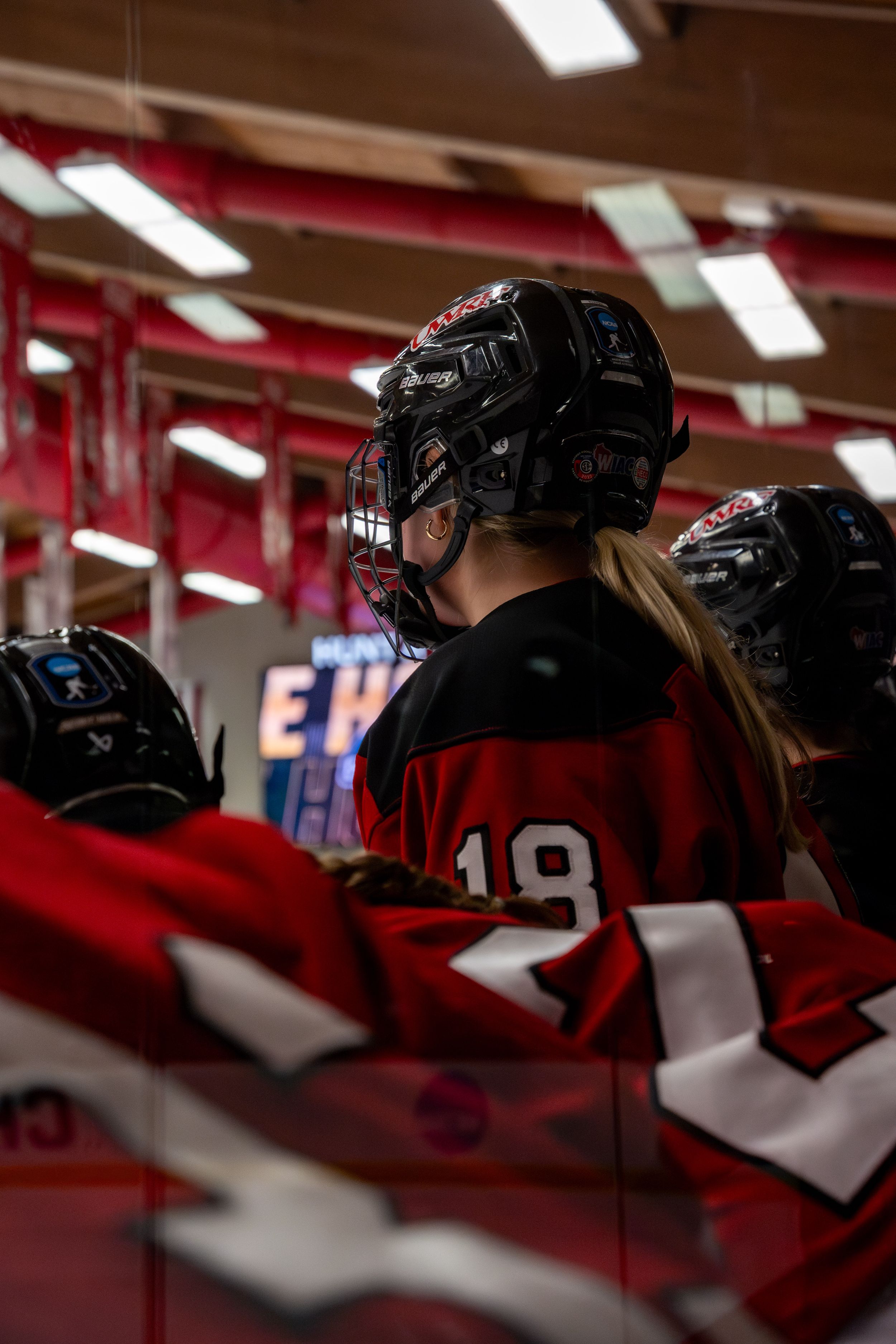 Ice hockey players in red jerseys sit on the bench wearing black helmets during a game inside an arena.