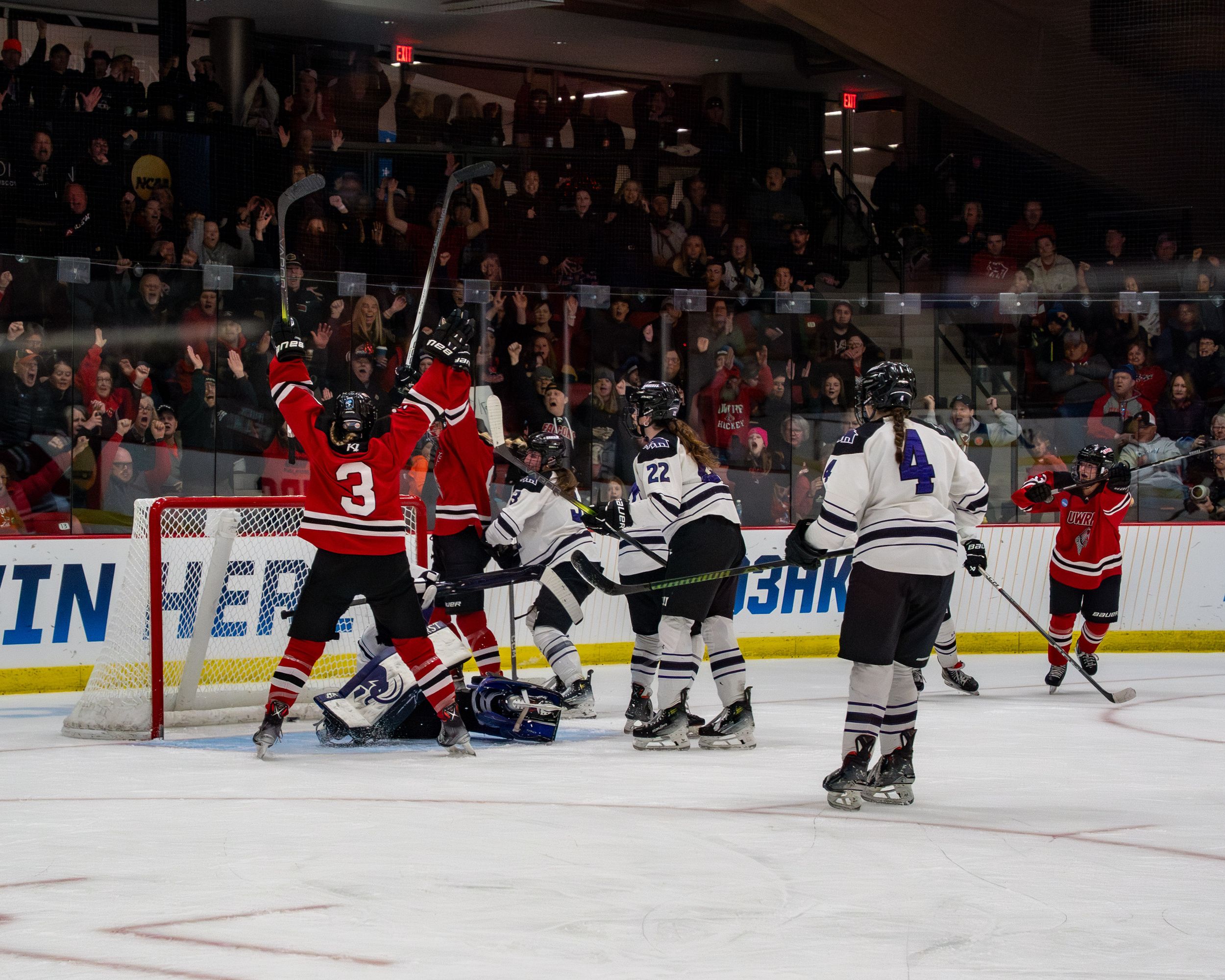Multiple hockey players crowd around the goal net during a scoring attempt in a competitive game.