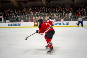 Hockey player in red jersey takes a shot on goal during game with crowded stadium in background at Augsburg arena.