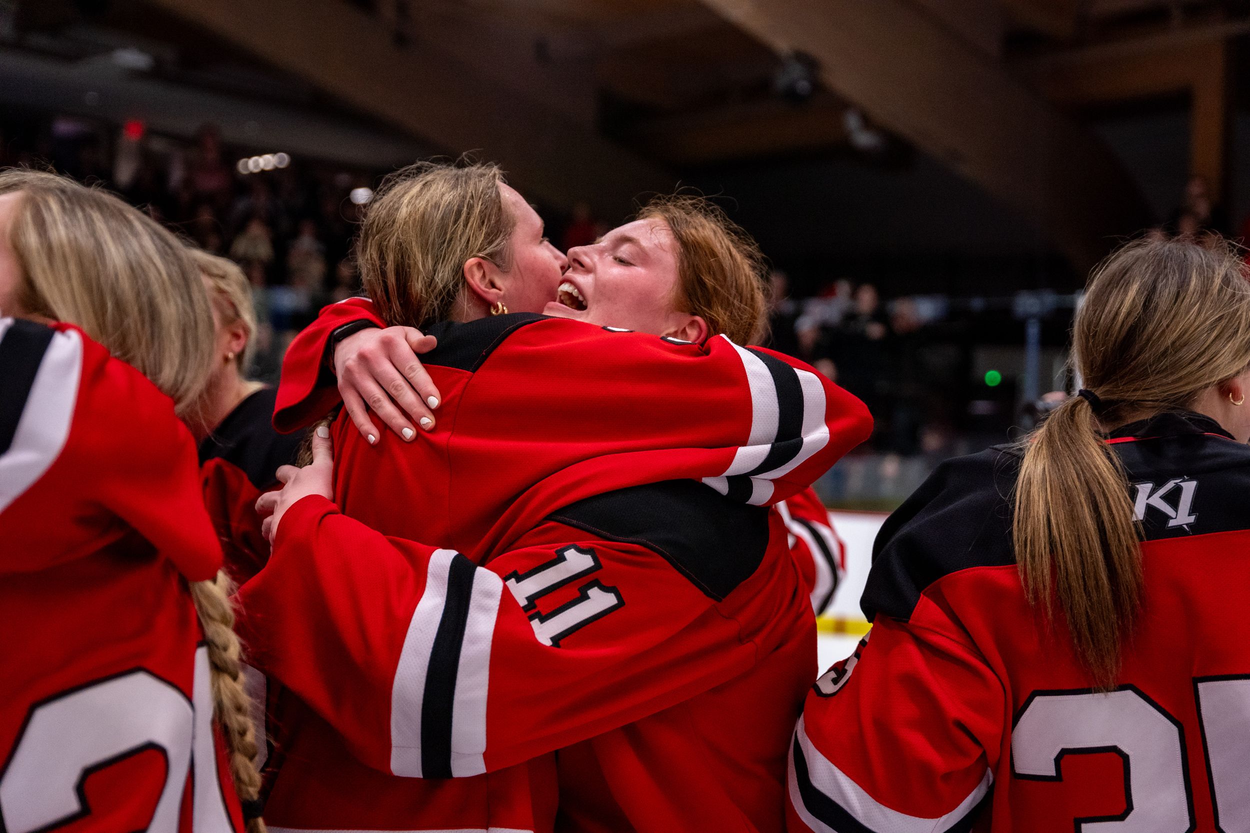 Two teammates in red hockey jerseys embrace in celebration during a game.