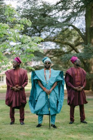Traditional African fashion showcased by three people wearing coordinated agbada robes and headwear outdoors.