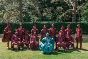 Group portrait of choir members in burgundy robes arranged in two rows outdoors.