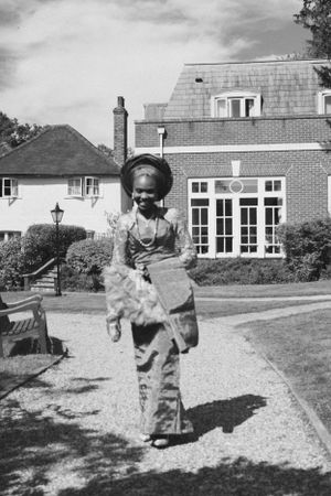 Vintage black and white photograph of someone walking on a path outside a brick house.