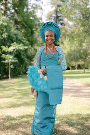 Traditional African attire in turquoise with matching gele headwrap and coral necklace.