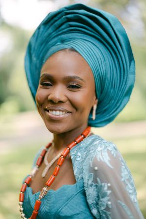 Elegant turquoise gele headwrap and coral necklace with lace-detailed dress.