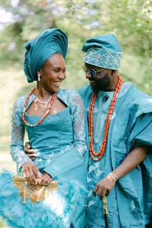 Couple in coordinating blue Nigerian formal wear with coral beads share an intimate moment in nature.