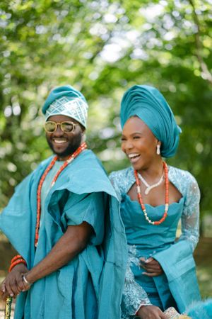 A couple in turquoise Nigerian wedding attire share a candid laughing moment.