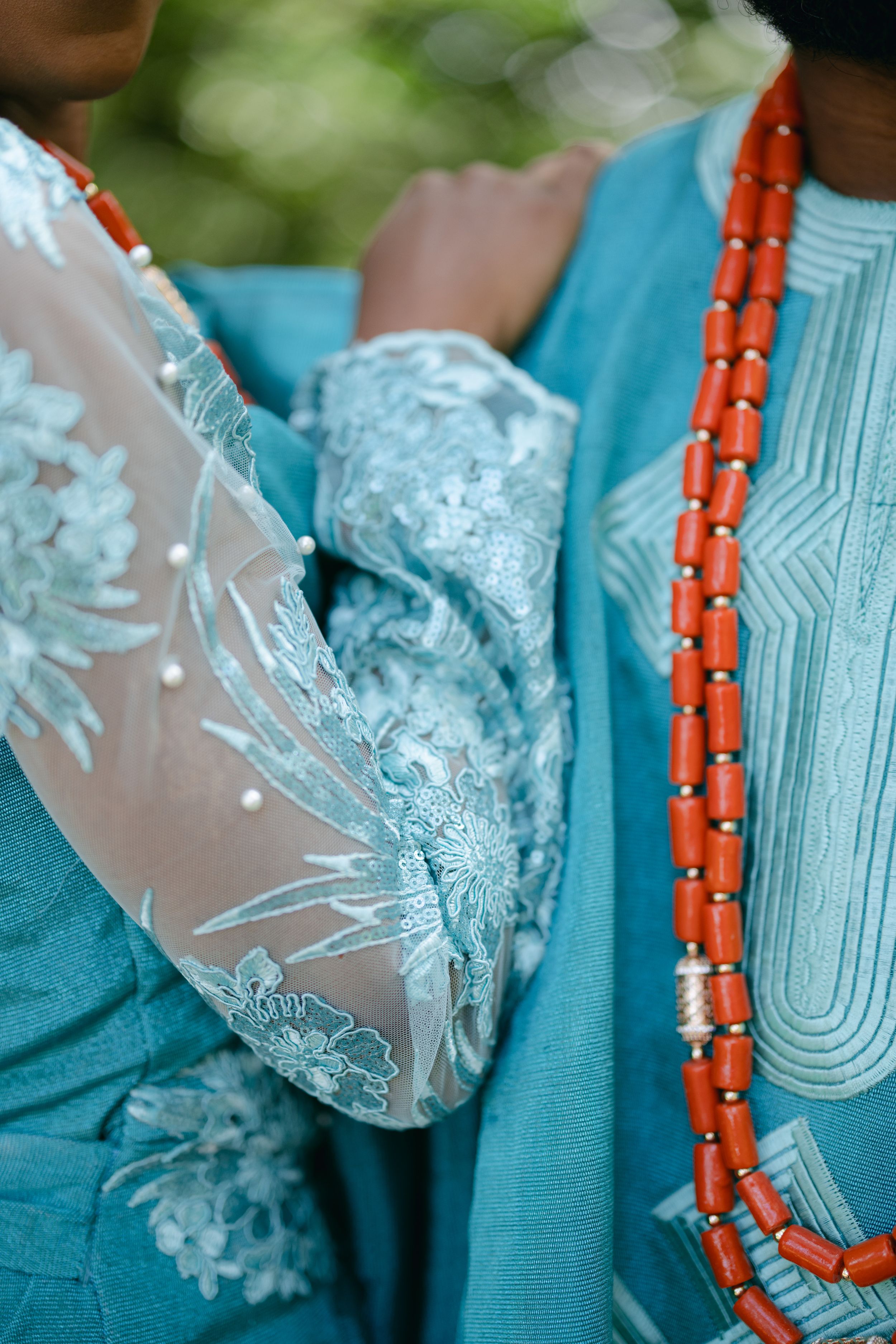 Detail shot of turquoise lace fabric and coral beaded necklace in traditional Nigerian attire.