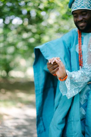 Traditional Nigerian attire in turquoise blue with detailed embroidery and geometric patterns shown in an outdoor setting.