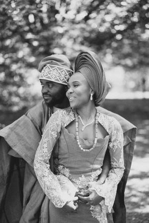 Black and white photo of a couple in traditional Nigerian wedding attire standing together outdoors.