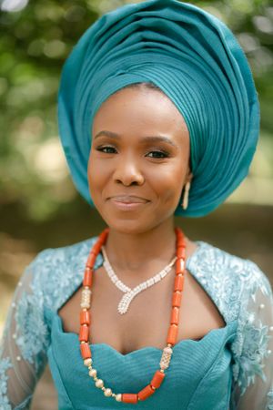 Traditional Nigerian bridal portrait featuring turquoise gele headwrap and coral beaded necklace.