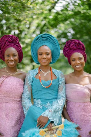 Close-up of three women in pink and turquoise traditional African attire with matching gele headwraps.