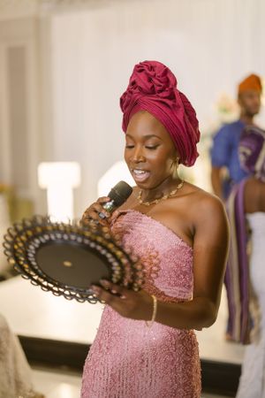 Woman in pink dress and burgundy headwrap holding decorative fan at formal event.