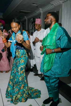Wedding guests dancing in colorful Nigerian attire featuring teal and green traditional garments.