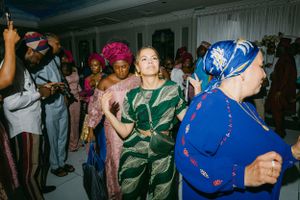 Celebrants in colorful traditional African attire dance and celebrate at an indoor gathering.