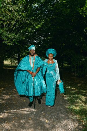 Two people in coordinating turquoise Nigerian attire walk together on a park path.