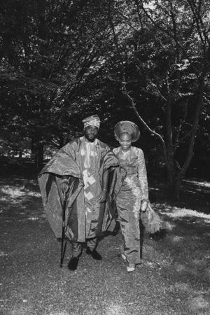 Black and white photo of two people in traditional African dress standing in a wooded area.