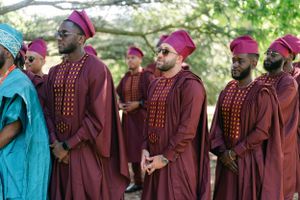 Group wearing burgundy robes and magenta caps stand in formation outdoors.