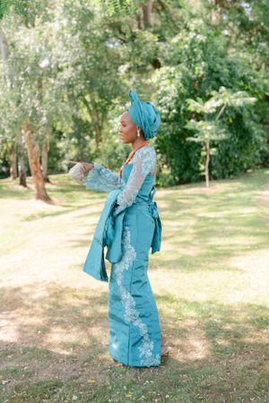 Traditional turquoise outfit with lace details and head wrap photographed in a sunny garden setting.