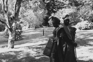 Black and white photograph of two people in formal attire standing in a park setting.