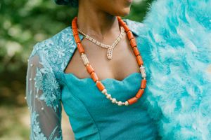 Close-up detail of turquoise lace dress with coral beaded necklace and feather accessory.