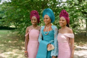 Three women in formal attire wearing gele headwraps in turquoise and pink colors.