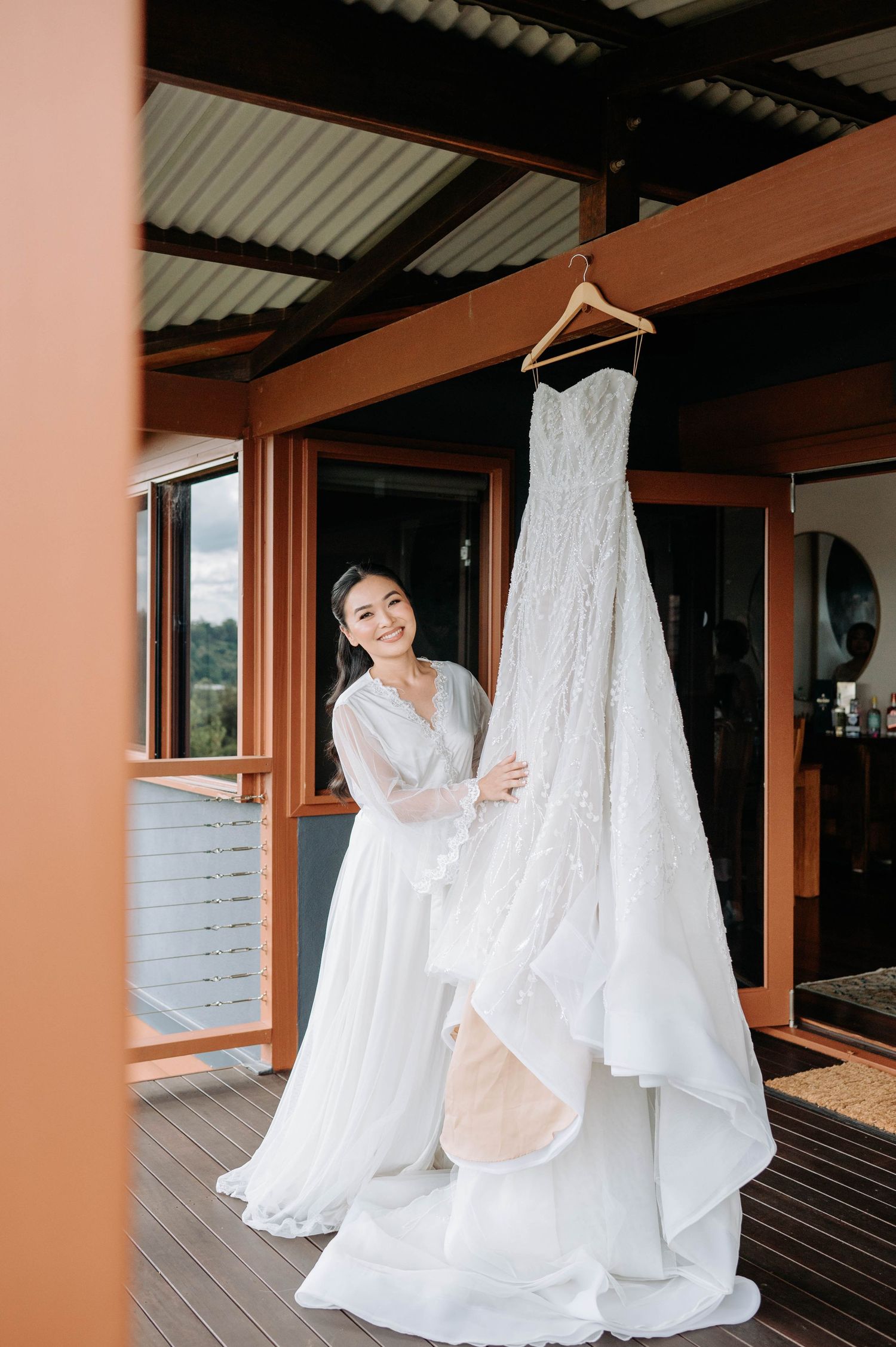 A beautiful white lace wedding dress hangs on display in sunlit room.