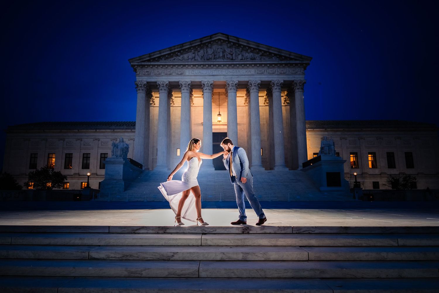 Elegant couple shares a romantic moment on the steps of the U.S. Supreme Court at night, beautifully illuminated against the deep blue sky.