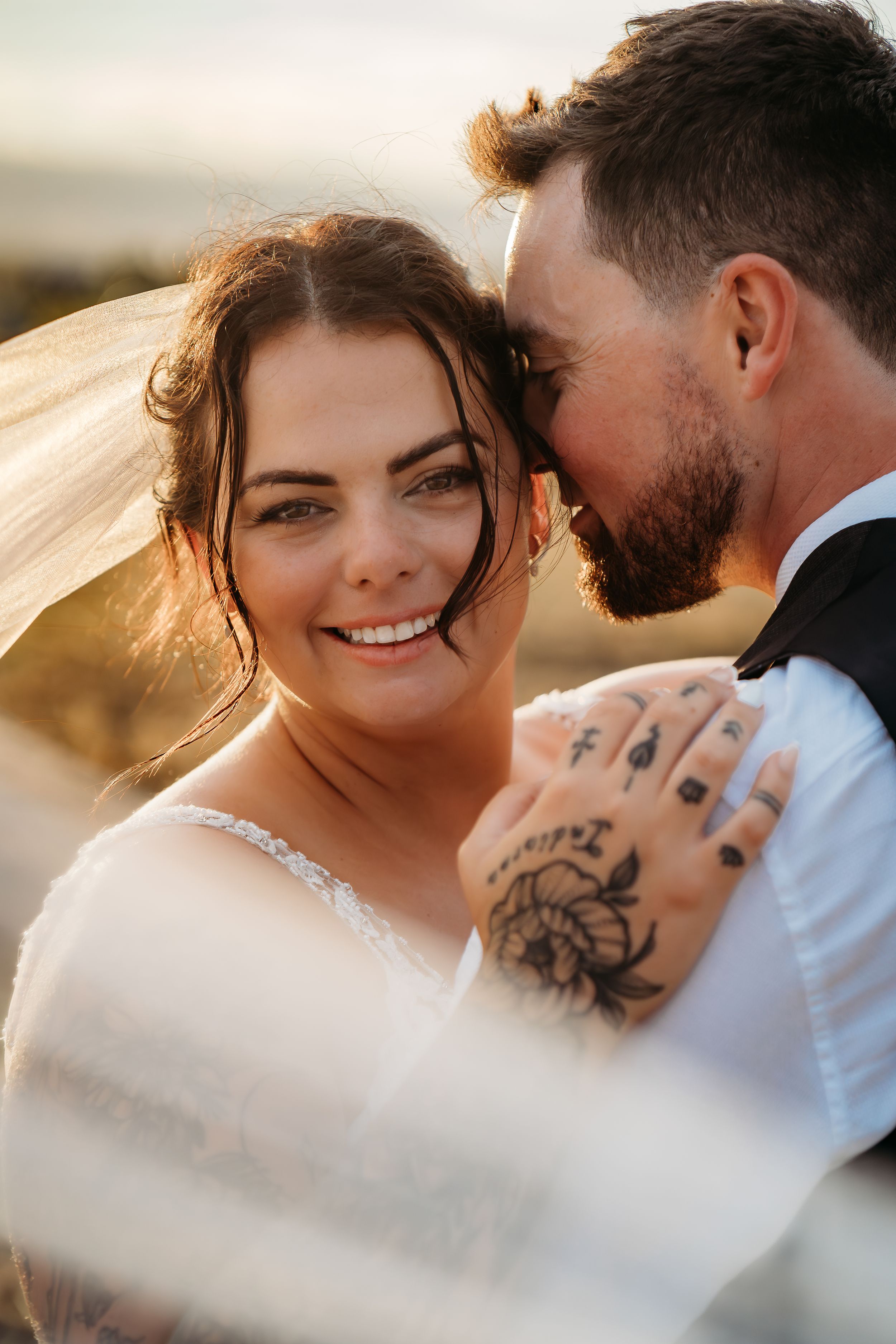 Intimate wedding portrait with visible tattoo art in warm sunlight.