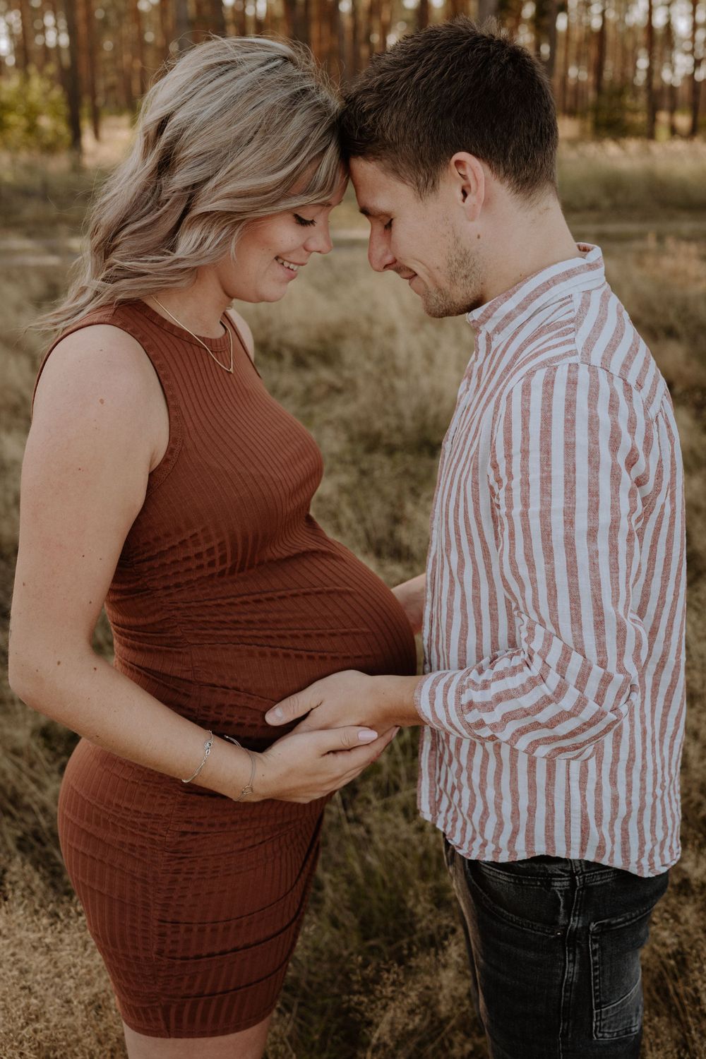 A couple sharing an intimate moment outdoors as they lovingly touch her pregnant belly in a rustic autumn setting.