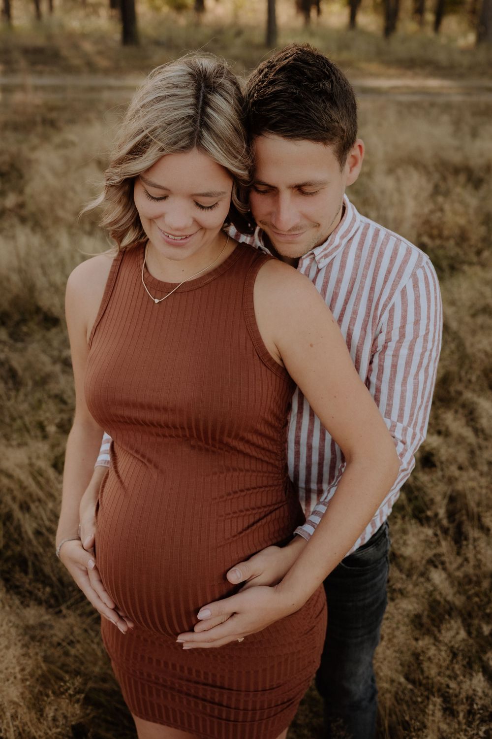 Couple embraces during maternity photoshoot in rustic outdoor setting.