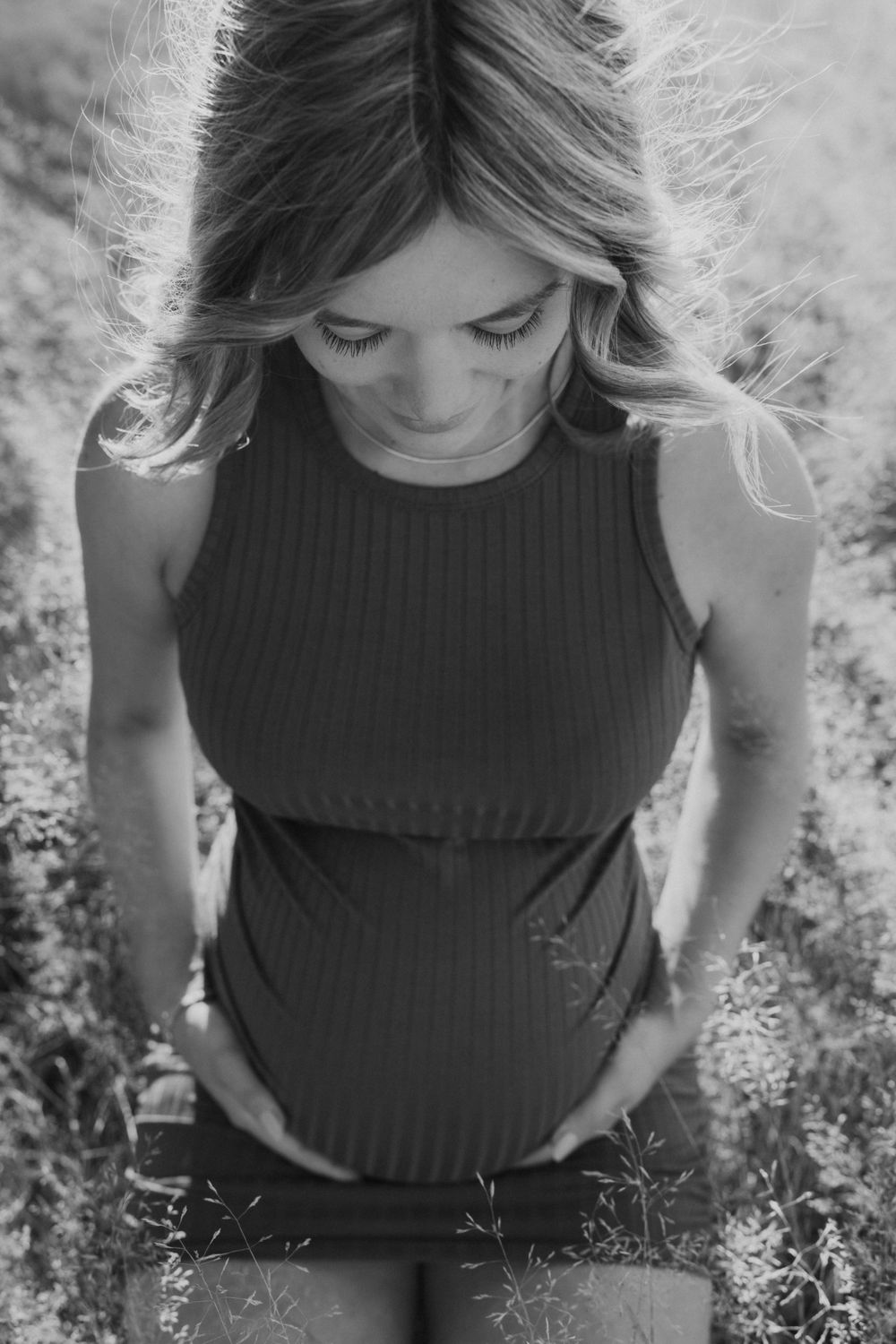 Woman in ribbed tank top poses for maternity photo in natural sunlight.