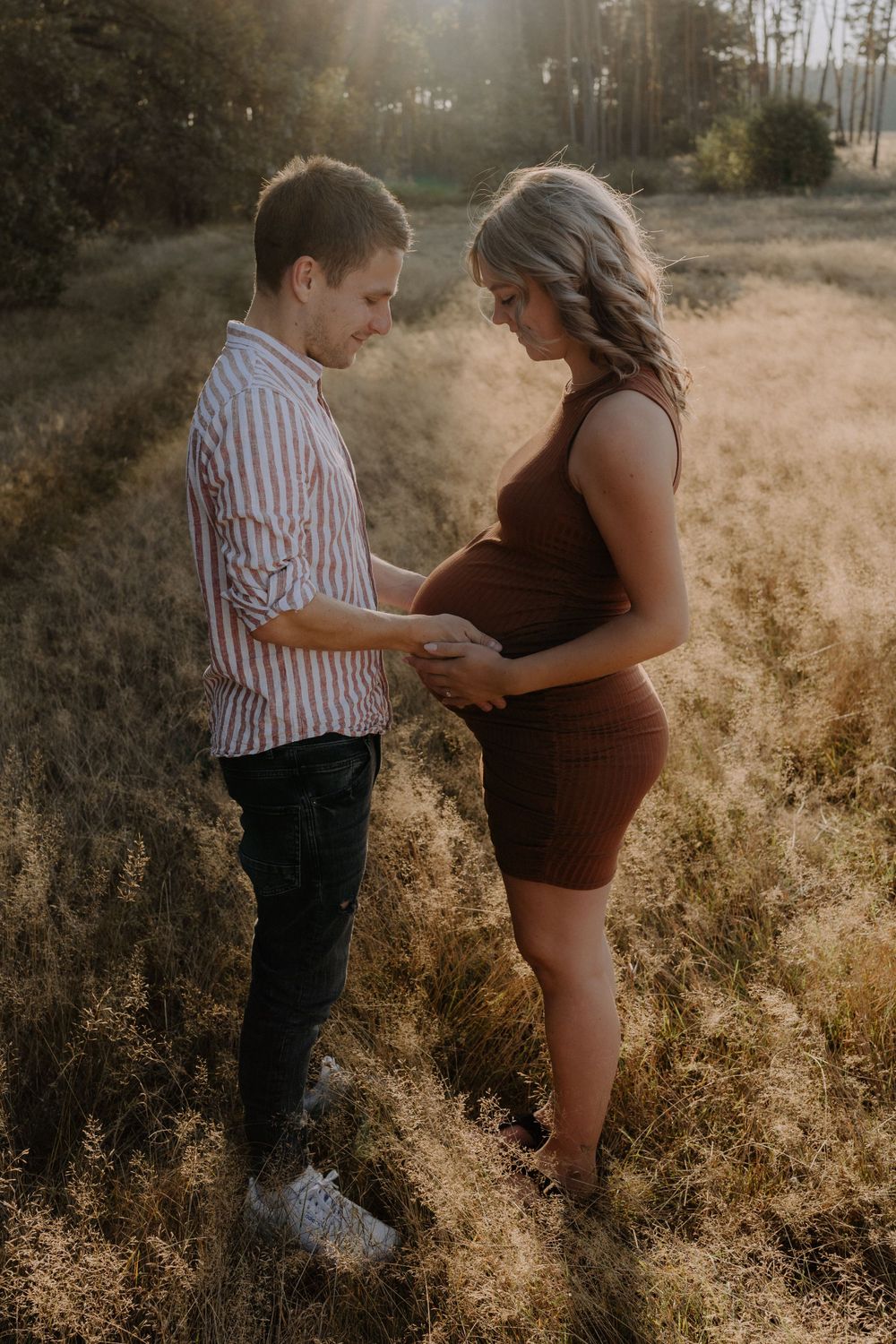 A romantic maternity photoshoot in a golden field during sunset with a couple sharing an intimate moment.