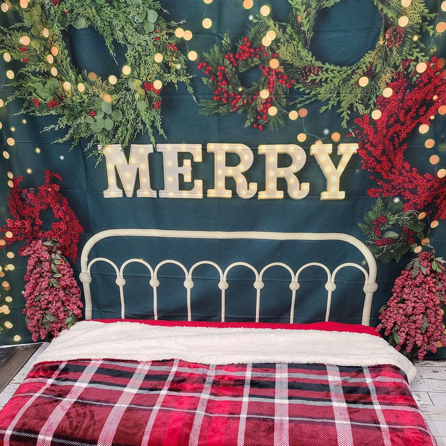 A festive bedding setup with MERRY letters, plaid blanket and Christmas greenery against a dark blue background.