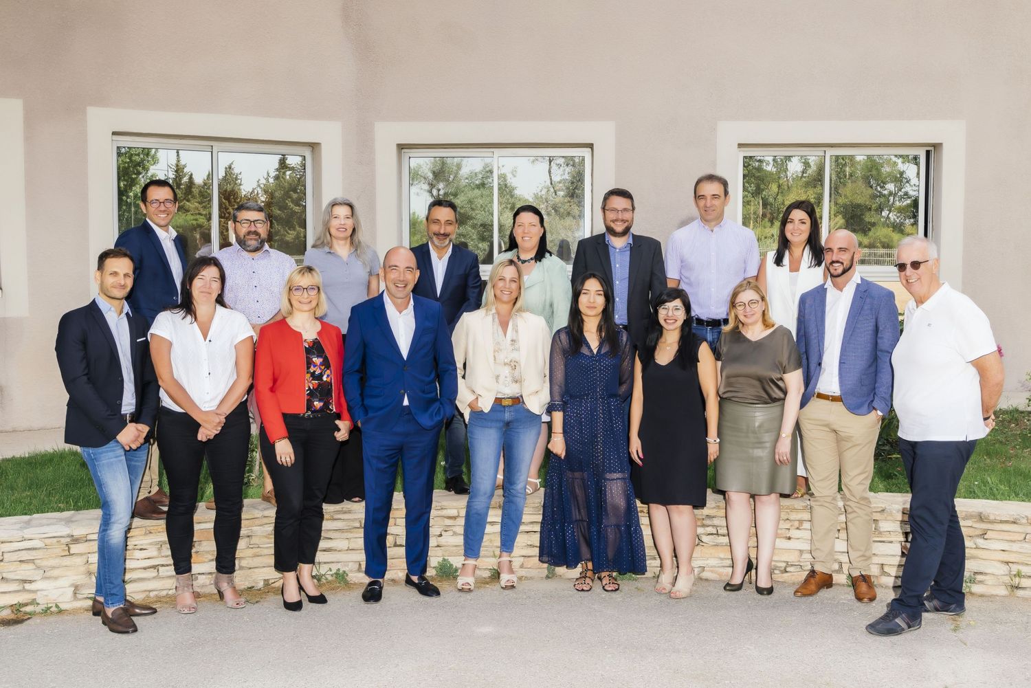 Professional group photo of business team members standing together outside building entrance in formal attire.