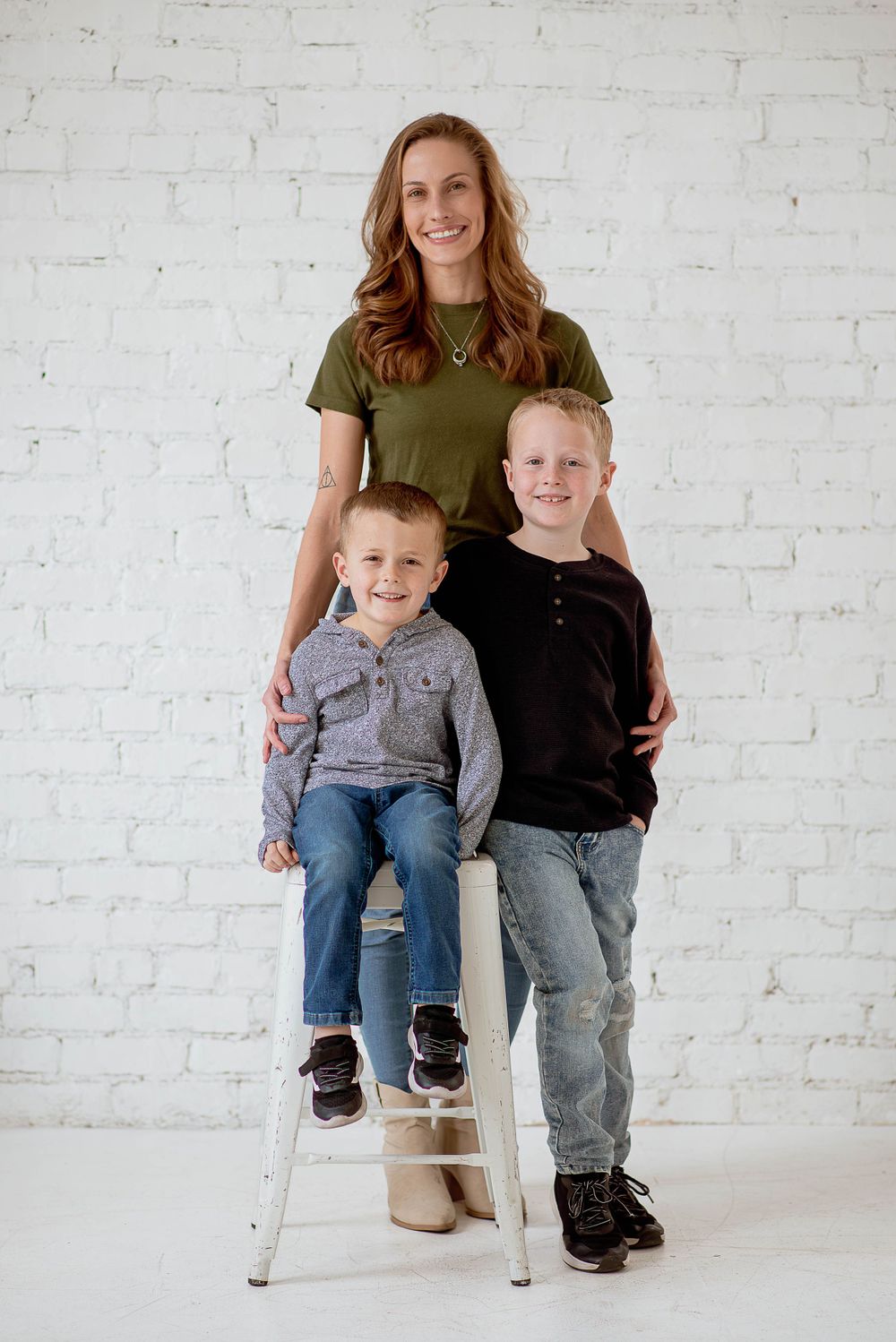 A family portrait against a white brick wall with a stool and casual clothing.