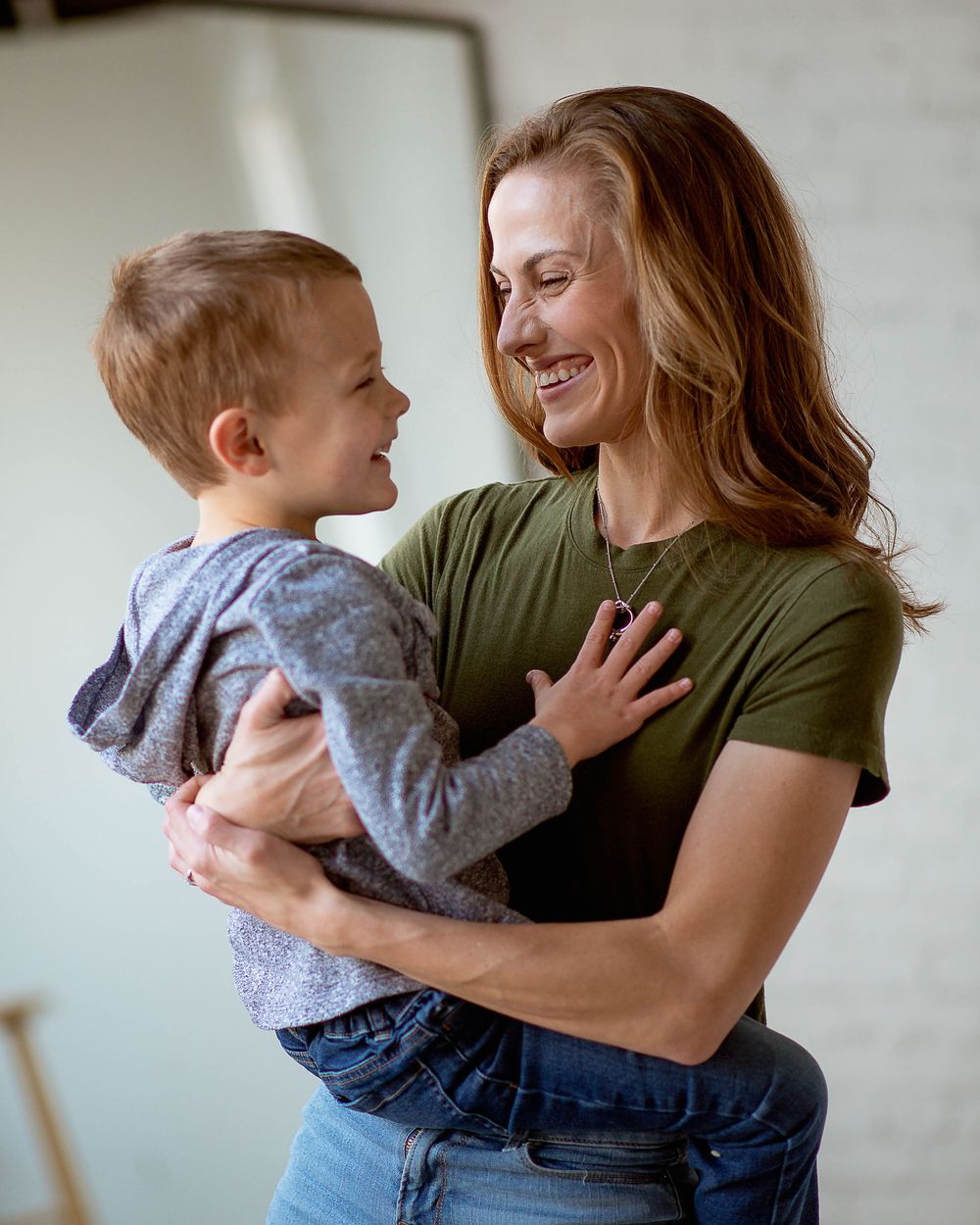 A joyful moment between a young child in a gray hoodie and an adult in a green t-shirt sharing laughter together.