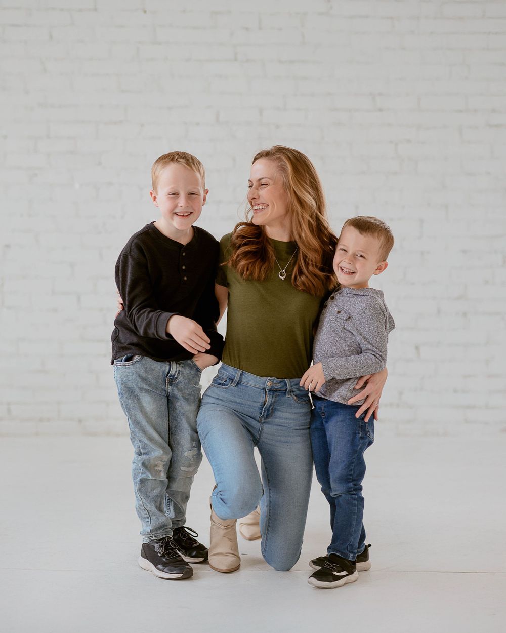 A candid family portrait against a white brick wall showing joyful interactions in casual denim and earth-toned outfits.