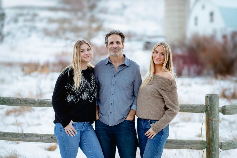 Family portrait in winter setting with rustic wooden fence and snowy background.