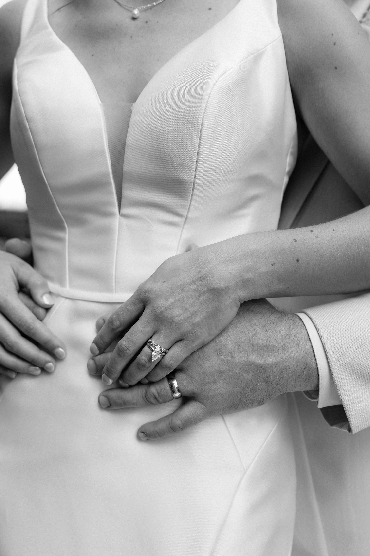 Intimate wedding moment under floral arch by waterfront in black and white.