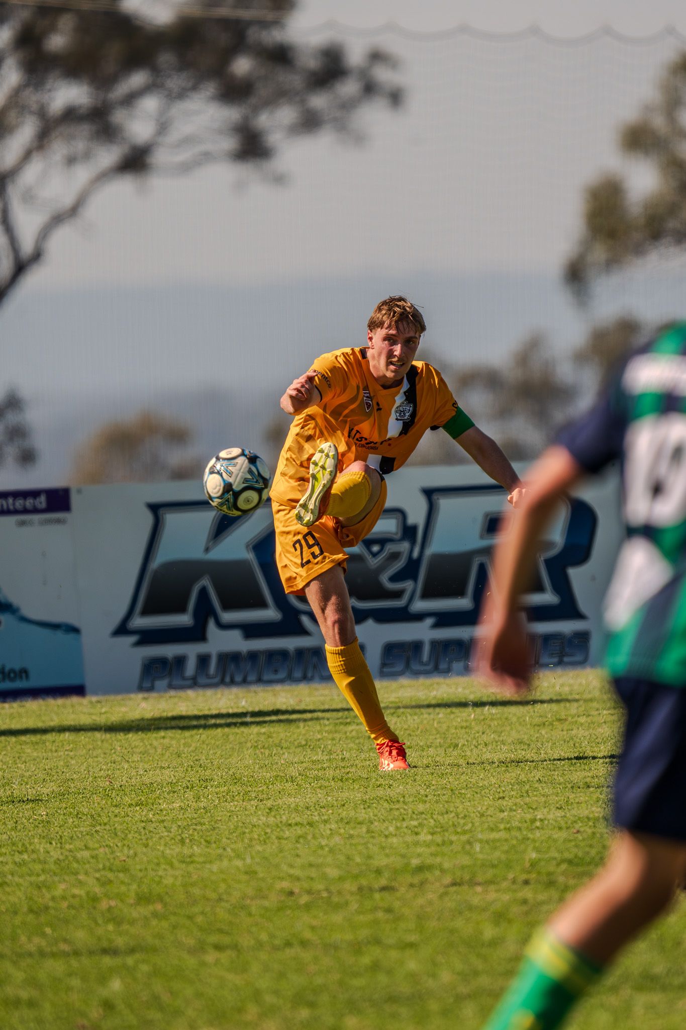 Soccer player in yellow uniform kicking ball during outdoor match.