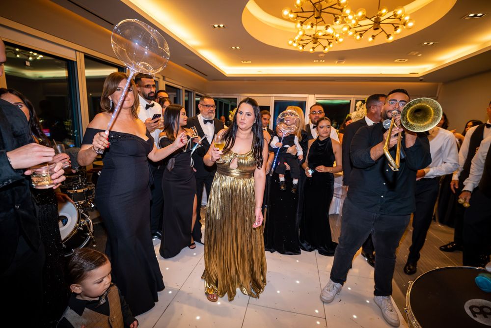 Wedding party dancing on a reception dance floor under elegant lighting with people in formal attire.