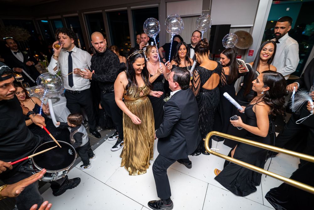 Energetic wedding reception with guests dancing and celebrating around newlyweds on a white dance floor.