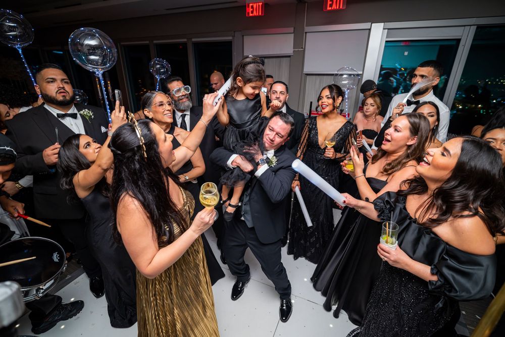 Wedding celebration with guests cheering and celebrating on a dance floor amid festive lighting.
