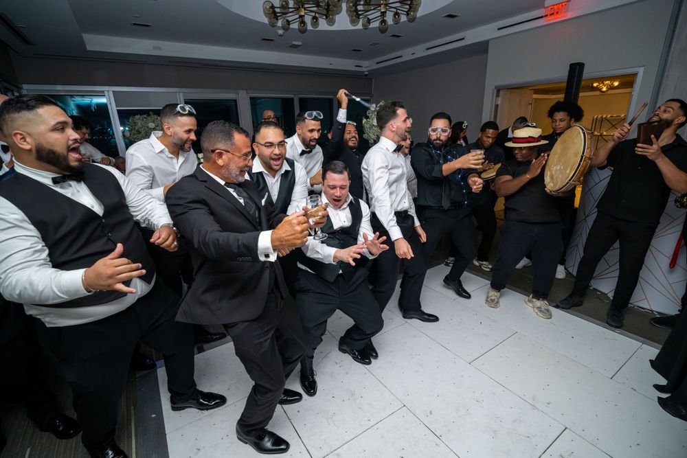 Groomsmen perform choreographed dance routine during wedding reception on white dance floor.