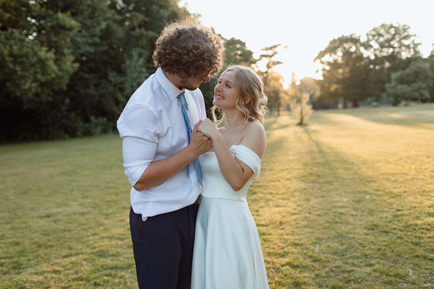 Young newly wed couple embracing with hands intertwined. The sunset is shining through the trees and the bride is smiling from ear to ear